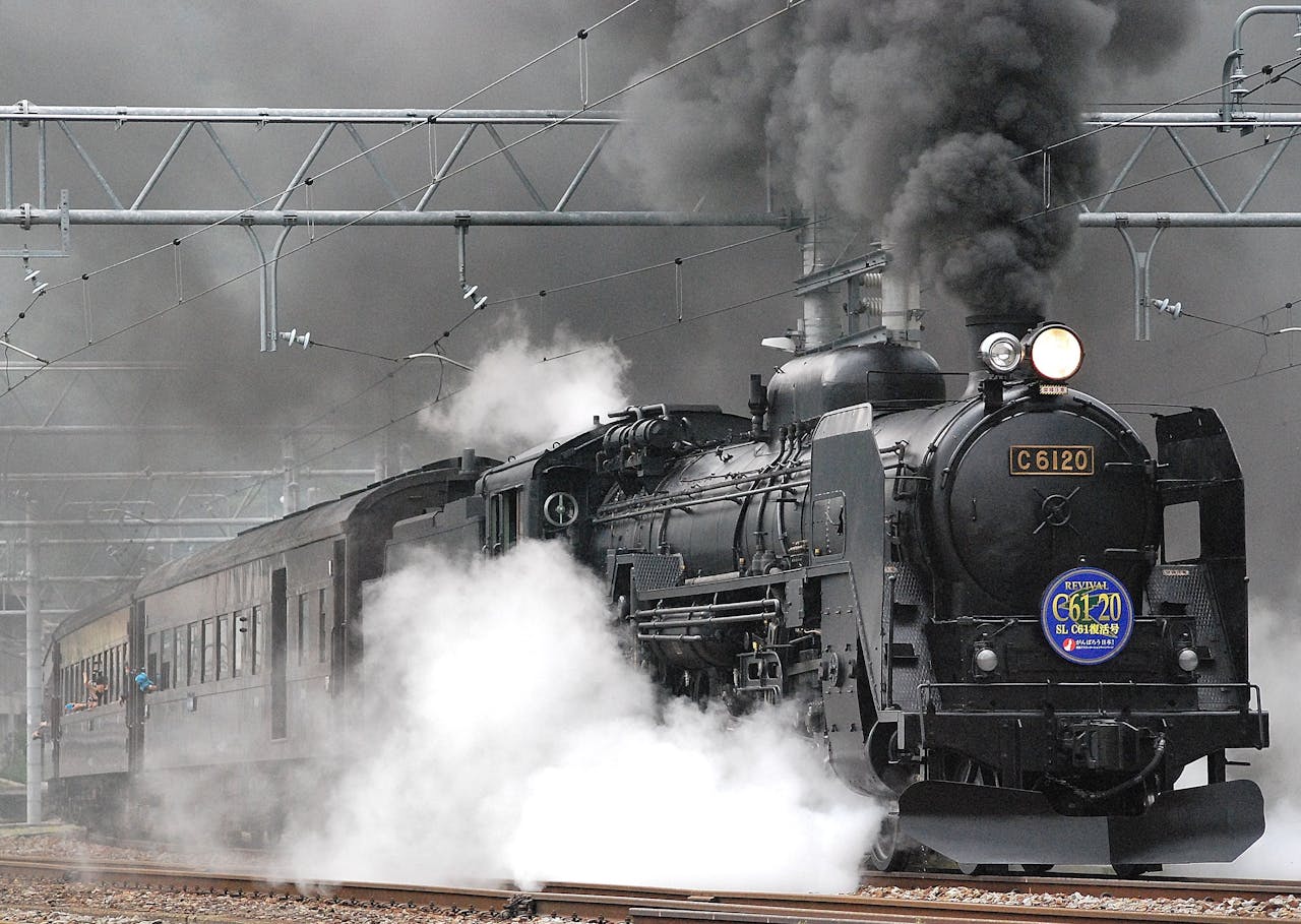 Steam locomotive releasing smoke and steam on a rail track, showcasing vintage train transportation.